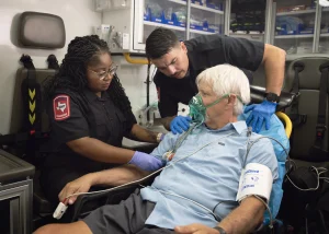 Image of two EMT workers inside a workstation taking care of a patient with o2 mask on.