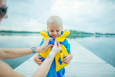 A mother is helping her son put on a life jacket. He is about to go swimming.