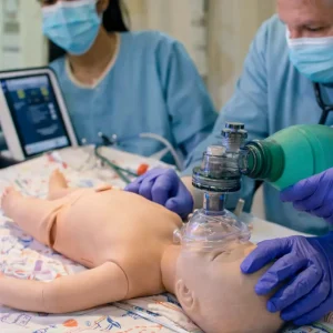 neonatal-resuscitation-program-certified-health-street-houston-texas Healthcare team practicing neonatal resuscitation program skills on an infant mannequin, using an Ambu bag and tablet with NRP learning platform login during NRP training for NRP certification near me in Houston.