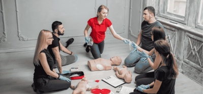Corporate CPR Training Houston: RQI vs Live RQI vs instructor-led CPR course in Houston showing team practicing BLS and AED skills on adult and infant manikins during live classroom training session.